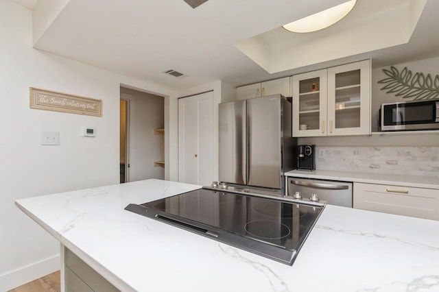 kitchen with stainless steel appliances, light hardwood / wood-style floors, light stone counters, and decorative backsplash