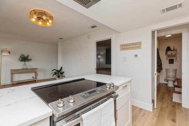 kitchen with stainless steel electric range oven, light stone countertops, white cabinets, and light wood-type flooring