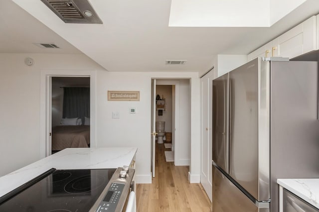 kitchen featuring light stone counters, stainless steel appliances, light wood-type flooring, and white cabinets