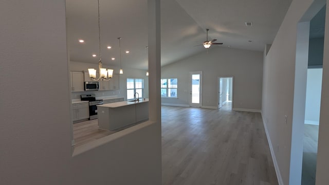 kitchen with light hardwood / wood-style flooring, appliances with stainless steel finishes, a kitchen island, pendant lighting, and ceiling fan with notable chandelier