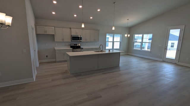 kitchen featuring sink, appliances with stainless steel finishes, a kitchen island with sink, hanging light fixtures, and a notable chandelier