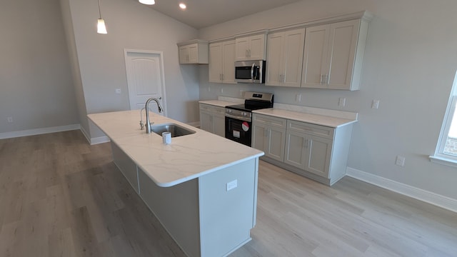 kitchen with sink, hanging light fixtures, a kitchen island with sink, light stone counters, and stainless steel appliances