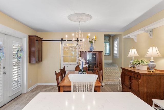 dining space with wood-type flooring, a barn door, and an inviting chandelier