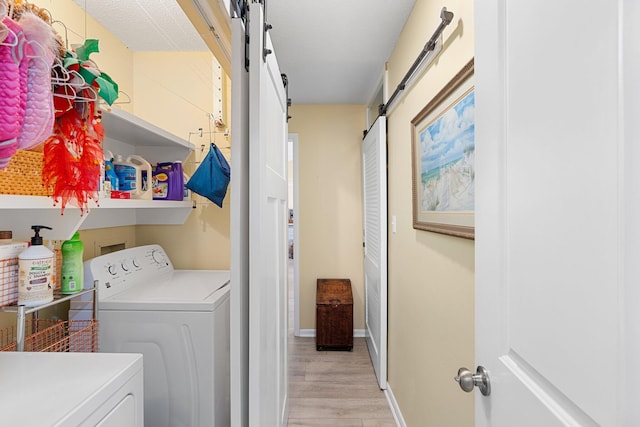 clothes washing area with separate washer and dryer, a barn door, and light wood-type flooring