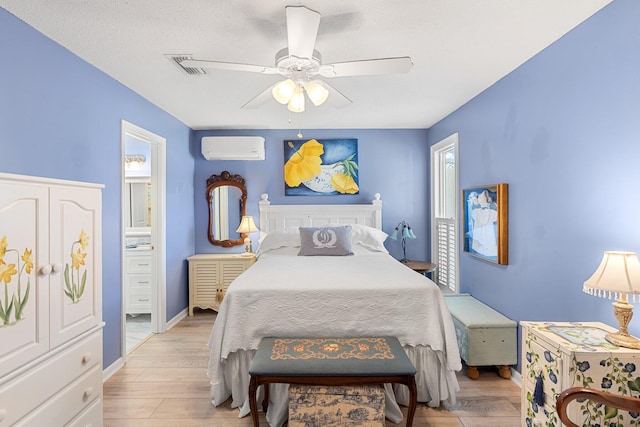 bedroom featuring ceiling fan, connected bathroom, light hardwood / wood-style floors, and a wall unit AC