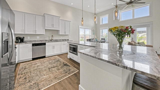 kitchen with pendant lighting, sink, white cabinetry, stainless steel appliances, and light stone countertops