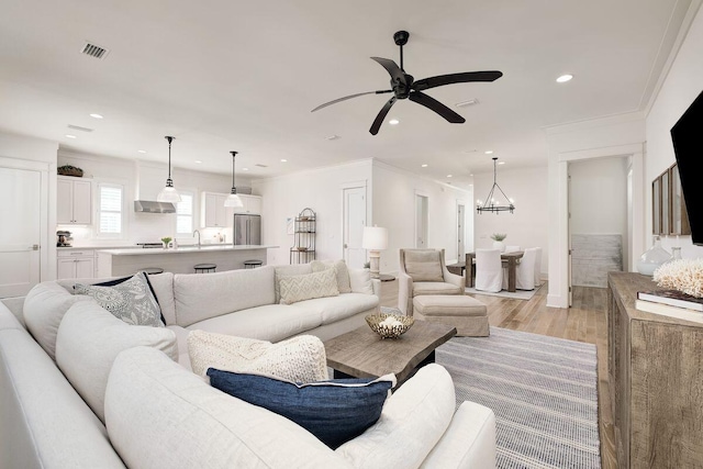 living room with ornamental molding, sink, ceiling fan with notable chandelier, and light wood-type flooring