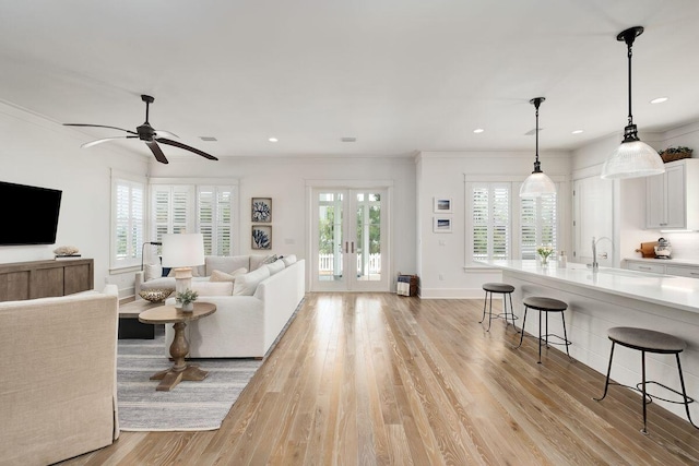 living room featuring sink, crown molding, light hardwood / wood-style flooring, ceiling fan, and french doors