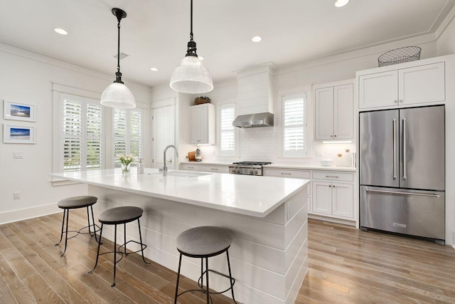 kitchen with sink, high end fridge, a center island with sink, and white cabinets