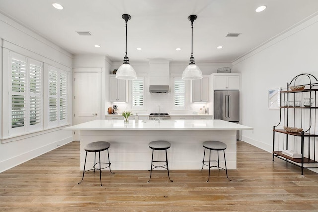 kitchen featuring high quality fridge, a breakfast bar area, a center island with sink, and white cabinets