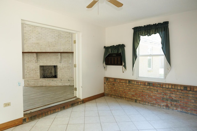 spare room with light tile patterned floors, a fireplace, ceiling fan, and brick wall