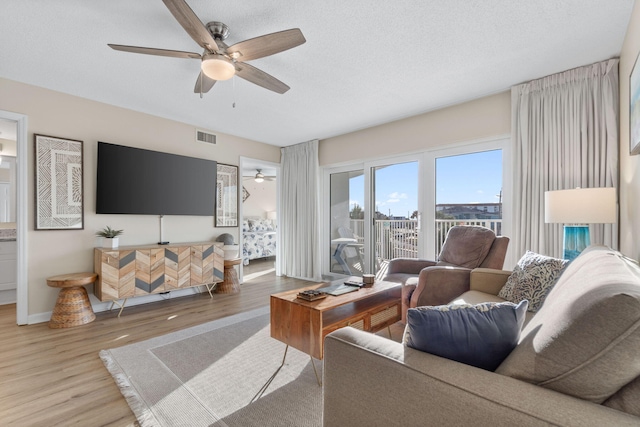 living room featuring ceiling fan, a textured ceiling, and light hardwood / wood-style floors