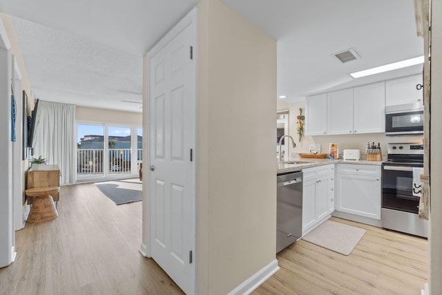 kitchen featuring appliances with stainless steel finishes, white cabinetry, sink, light hardwood / wood-style floors, and light stone countertops