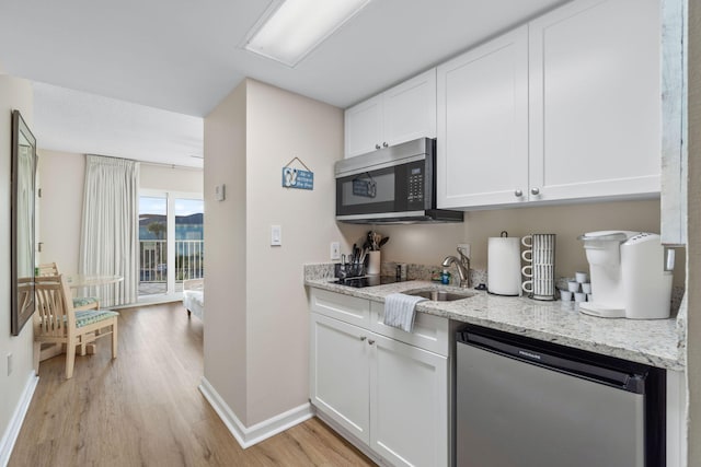 kitchen with light stone counters, dishwashing machine, light hardwood / wood-style flooring, and white cabinets