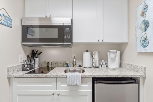 bar featuring light stone counters, stainless steel appliances, sink, and white cabinets