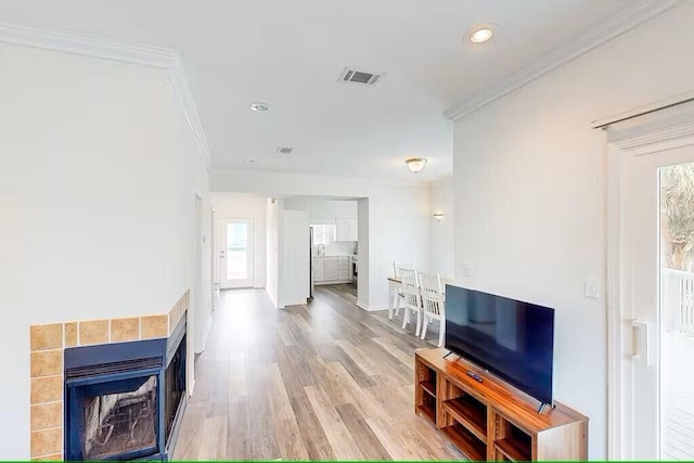 living room featuring a tiled fireplace, crown molding, and light hardwood / wood-style flooring