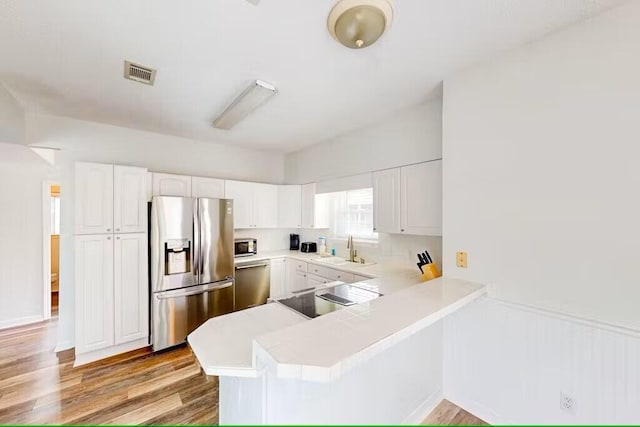 kitchen featuring sink, kitchen peninsula, white cabinets, and appliances with stainless steel finishes