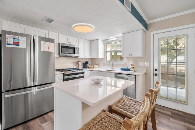 kitchen with sink, a breakfast bar, appliances with stainless steel finishes, white cabinetry, and a kitchen island