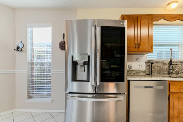 kitchen with brown cabinetry, appliances with stainless steel finishes, light countertops, a healthy amount of sunlight, and a sink