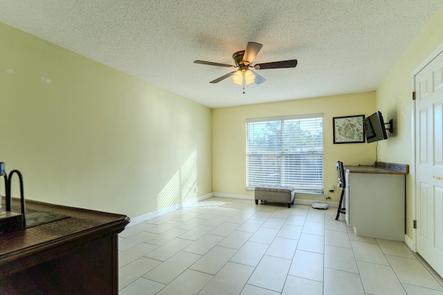 interior space featuring ceiling fan, a textured ceiling, baseboards, and light tile patterned floors