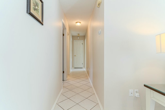 hallway featuring a textured ceiling, baseboards, and light tile patterned floors