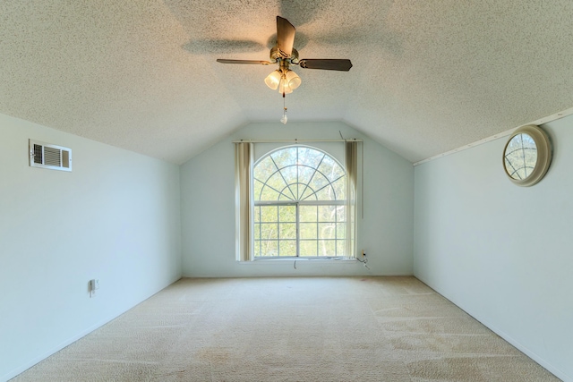 additional living space with lofted ceiling, a textured ceiling, visible vents, and light colored carpet