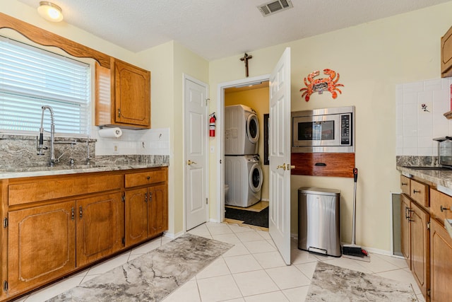 kitchen with visible vents, stainless steel microwave, stacked washer / drying machine, light countertops, and a sink