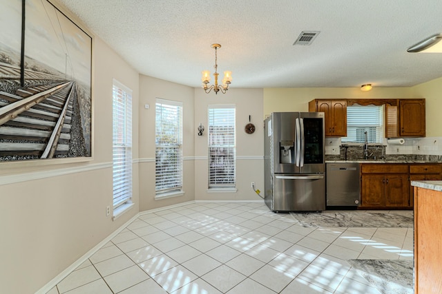 kitchen with stainless steel appliances, pendant lighting, brown cabinetry, and visible vents