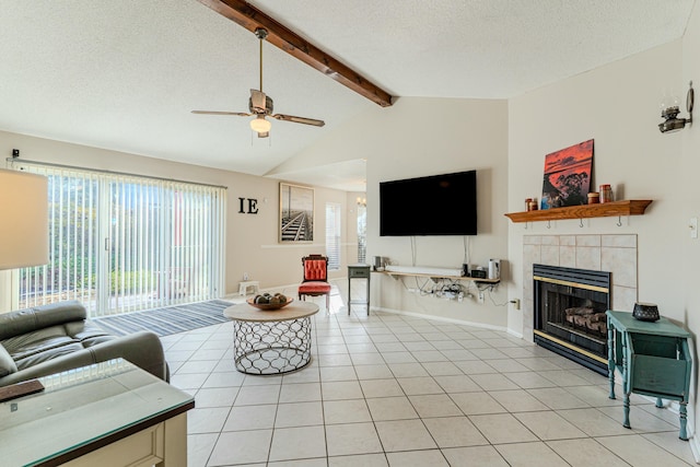 living area with vaulted ceiling with beams, light tile patterned floors, a tiled fireplace, ceiling fan, and a textured ceiling