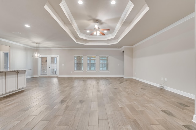 unfurnished living room with a raised ceiling, ornamental molding, ceiling fan with notable chandelier, and light wood-type flooring