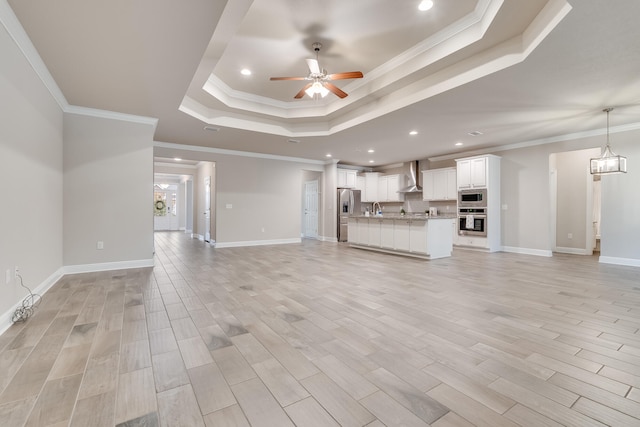 unfurnished living room featuring sink, crown molding, a tray ceiling, light hardwood / wood-style floors, and ceiling fan with notable chandelier