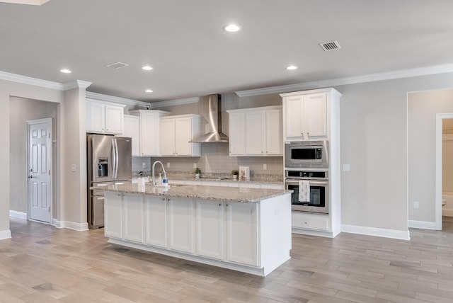 kitchen with white cabinets, appliances with stainless steel finishes, an island with sink, and wall chimney range hood