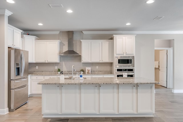 kitchen featuring wall chimney exhaust hood, sink, a center island with sink, appliances with stainless steel finishes, and white cabinets