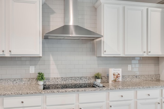 kitchen with white cabinetry, wall chimney range hood, light stone counters, and decorative backsplash