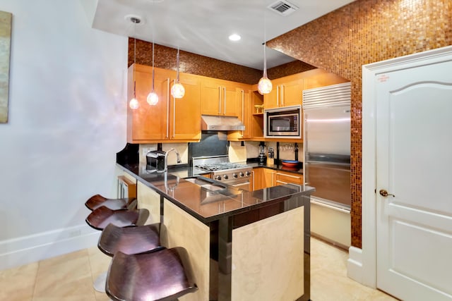 kitchen featuring light tile patterned floors, a breakfast bar area, hanging light fixtures, built in appliances, and kitchen peninsula