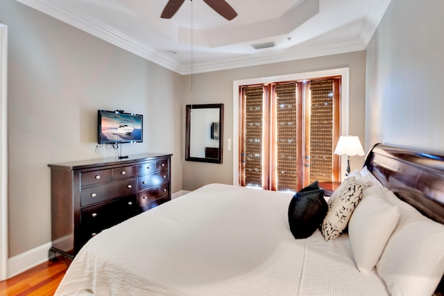 bedroom with crown molding, a tray ceiling, ceiling fan, and light hardwood / wood-style flooring