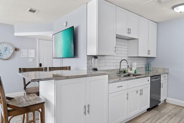 kitchen with sink, white cabinets, a kitchen bar, stainless steel dishwasher, and light stone counters