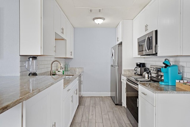 kitchen with sink, white cabinetry, light stone counters, appliances with stainless steel finishes, and light hardwood / wood-style floors