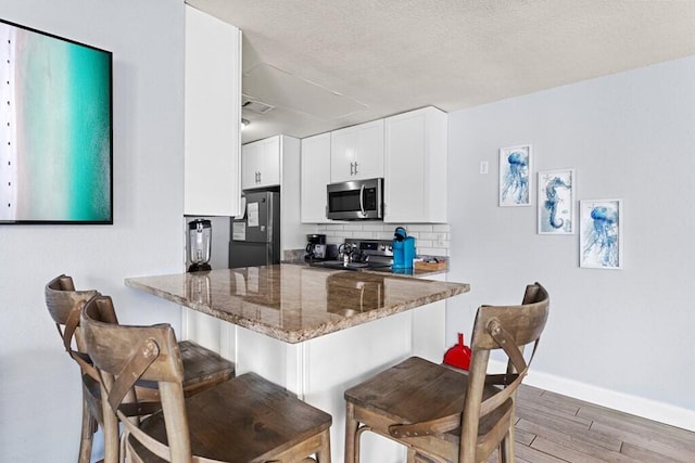 kitchen with a breakfast bar, white cabinetry, appliances with stainless steel finishes, kitchen peninsula, and dark stone counters