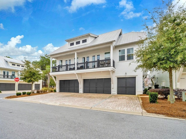 view of front facade with decorative driveway, metal roof, a balcony, and an attached garage