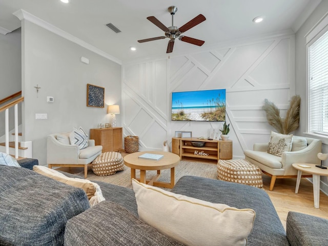 living room featuring light wood-style flooring, a decorative wall, visible vents, ornamental molding, and stairway