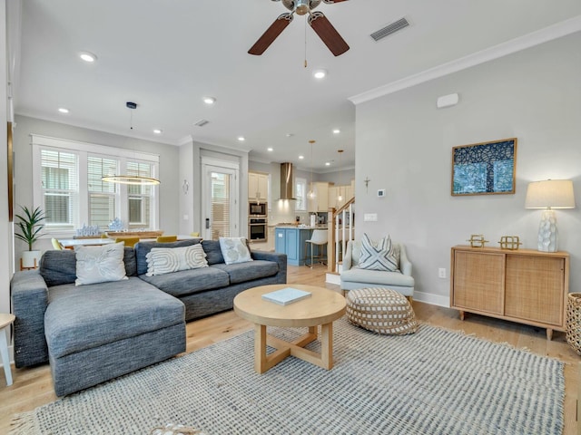 living area featuring light wood-type flooring, stairway, visible vents, and crown molding