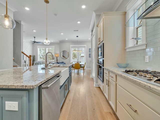 kitchen with light stone counters, decorative light fixtures, a spacious island, appliances with stainless steel finishes, and light wood-type flooring