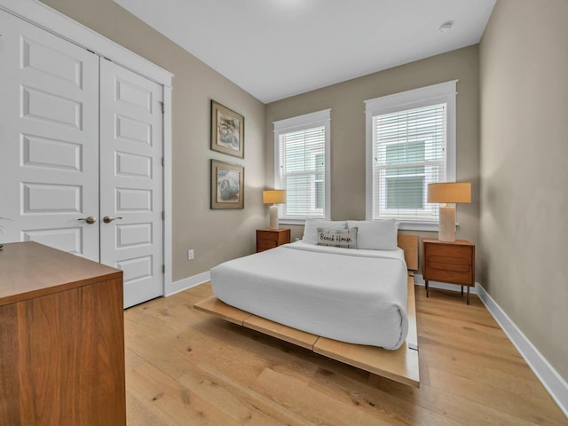 bedroom with a closet, baseboards, and light wood finished floors