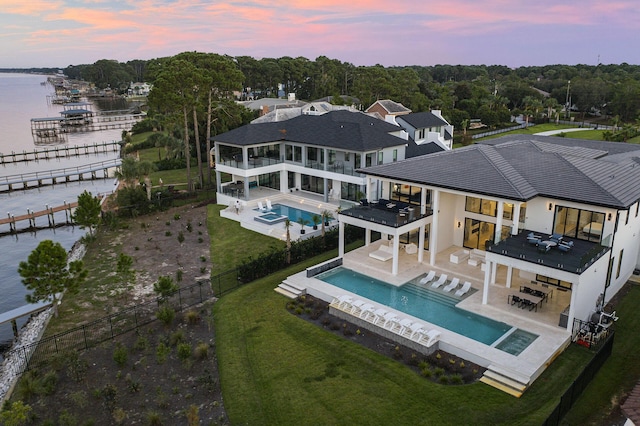 back house at dusk with a patio area, an in ground hot tub, and a water view