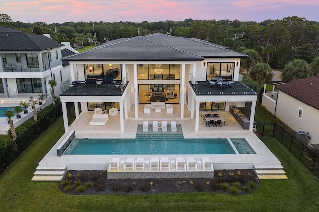 back house at dusk with a pool with hot tub, an outdoor hangout area, a patio area, and a balcony