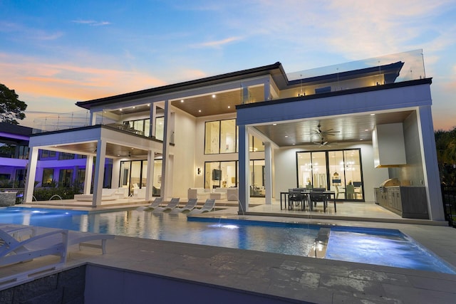 back house at dusk featuring pool water feature, area for grilling, ceiling fan, and a pool with hot tub