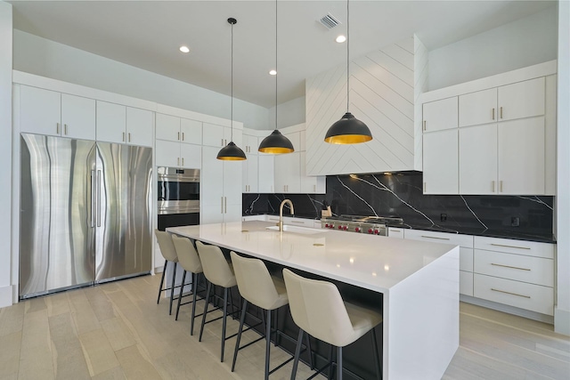 kitchen with sink, white cabinetry, decorative light fixtures, stainless steel fridge, and an island with sink