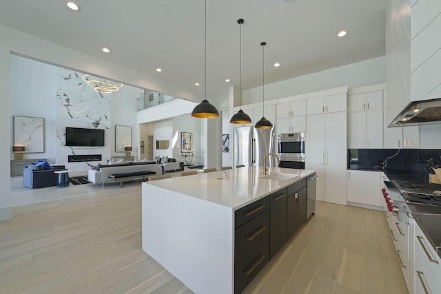 kitchen featuring hanging light fixtures, an island with sink, ventilation hood, and white cabinets