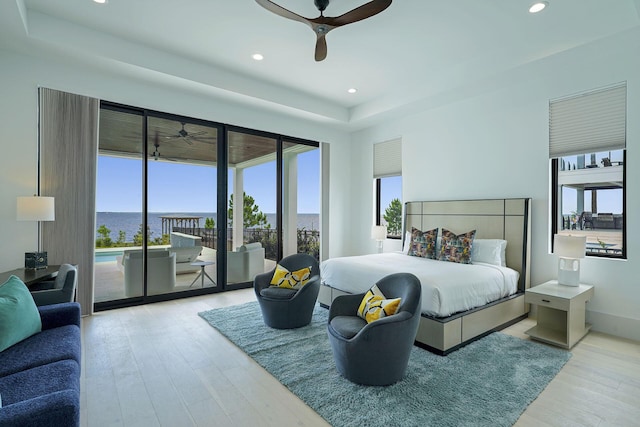 bedroom featuring a raised ceiling, a water view, access to exterior, and light hardwood / wood-style floors